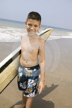 Portrait of boy holding surfboard on beach