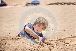 Portrait of a boy playing on the beach buried in the sand