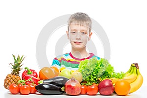 Portrait of a boy at the table with a pile of fresh vegetables and fruits isolated