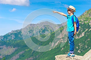 Portrait of a boy traveler standing on a rock and pointing