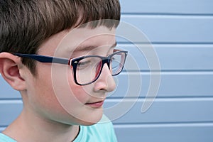 A portrait of a boy wearing glasses against grey blue plank painted wall with copy space, myopia, astigmatism and ophthalmologic