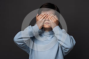 Portrait of boy 10-12 years old covering his eyes with hands. Facial expression concept. Studio shot, white background