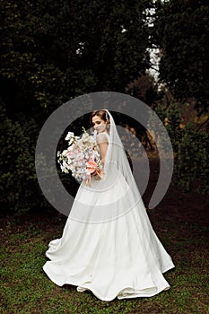 Portrait of the bride. Attractive young girl look at the camera in a white wedding dress and veil holding a bouquet of