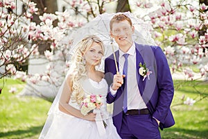 Portrait of a bride and groom in a park with white lace parasol