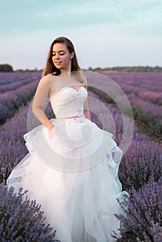 Portrait of the bride in a lavender field of flowers dressed in a white dress. Girl in the lavender bushes in summer