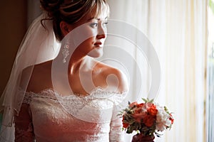 Portrait of bride in profile with wedding bouquet next to window.