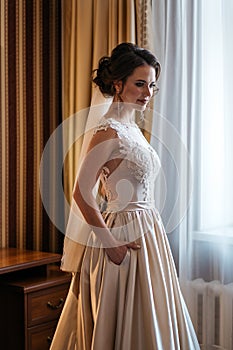 Portrait of a bride in a wedding dress standing near window