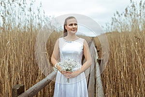 Portrait of a bride in a white long wedding dress with a white small bouquet