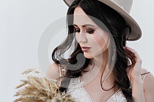 Portrait of the bride. A young attractive brunette woman with long black hair in braids. White wedding dress and beige