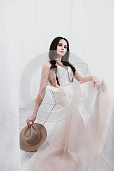 Portrait of bride. A young attractive brunette woman with long black hair in braids. White wedding dress and beige hat