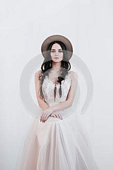 Portrait of bride. A young attractive brunette woman with long black hair in braids. White wedding dress and beige hat