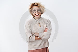 Portrait of bright and enthusiastic hipster girl wearing makeup and glasses holding hands crossed over chest as feeling