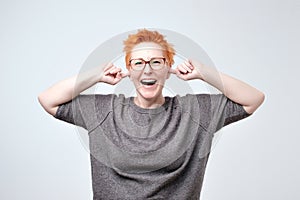 Portrait of bright mature caucasain woman with red hair covering ears with hands