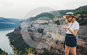 Portrait of brooding young girl with blonde hair in straw summer hat and hipster glasses on backdrop river natura mountain