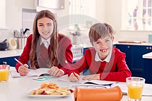 Portrait Of Brother And Sister Wearing School Uniform Doing Homework On Kitchen Counter