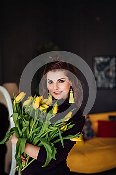 Portrait of a brown-haired woman with a bouquet of yellow tulips in her hands. on a dark background in the interior of