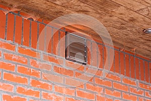 A portrait of a brown square design vent with closed slats placed in a red brick wall on a building for the air output of a cooker