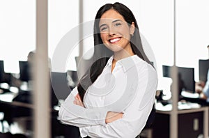 Portrait of a brunette business student in a modern technology office space, standing with arms folded, success concep