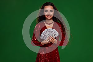 Portrait of a brunette curly woman in a glittered dress, holding fan folded money. Casino