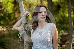 Portrait of a brunette female with a summer dress and red lipstick touching a tree trunk