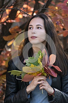 Portrait of brunette girl with autumn leaves in her hands. Beautiful young woman in forest. Vertical frame