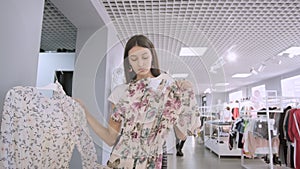 Portrait of a brunette girl in a clothing store in a mall. chooses between two dresses in front of a mirror. posing for