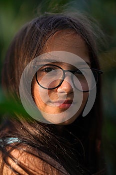 Portrait of a brunette girl wearing glasses on a green blurred background.