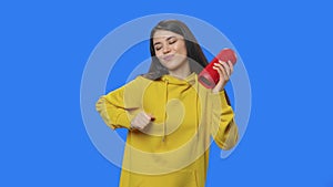 Portrait of brunette listening to music with bluetooth portable speaker and dancing. Young woman in yellow sweatshirt