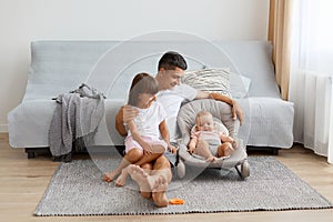 Portrait of brunette man wearing white casual style T-shirt and jeans short sitting on floor, little cute girl sitting on his legs