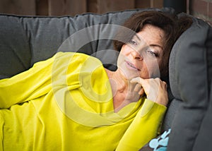 Portrait of brunette woman with dreamy look outdoors in garden. Woman middle aged lies on sofa in the garden