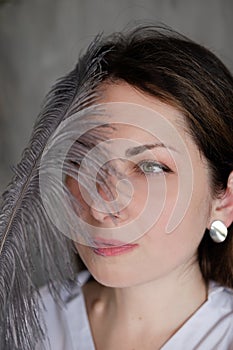 portrait of brunette woman girl holding big grey soft fluffy feather near face. Hair removal and Youth skin care concept