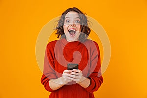 Portrait of brunette woman holding and using cell phone while standing isolated over yellow background