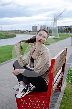 portrait of brunette woman with ponyrail sitting on a bench in park. nature lovers, attractive girl.