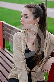 portrait of brunette woman with ponyrail sitting on a bench in park. nature lovers, attractive girl.