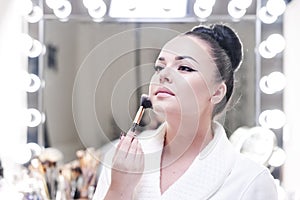 Portrait of a brunette woman putting on make up in front of the mirror