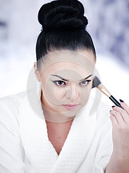 Portrait of a brunette woman putting on make up in front of the mirror