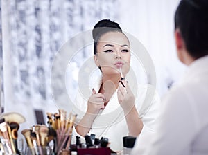 Portrait of a brunette woman putting on make up in front of the mirror