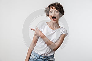 Portrait of brunette woman with short hair in basic t-shirt rejoicing and pointing finger at copyspace