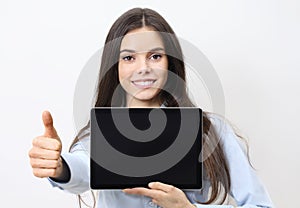Portrait of brunette young smiling woman holding a tablet with blank screen showing thumb up and looking at camera isolated on