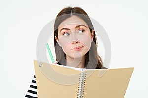 Portrait of brunette young woman, creative girl thinking, holding pen and notebook, making notes, writing in her diary