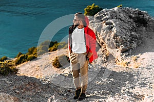 Portrait of a brutal bearded man in a red jacket by the sea. Male portrait on the background of a seascape.