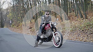 Portrait of brutal biker in sunglasses and leather on motorcycle on roadway