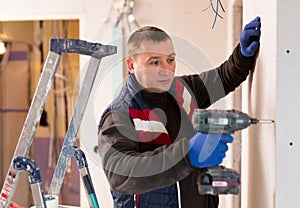 Portrait of builder handyman working with electric drill in repairable room