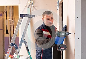 Portrait of builder handyman working with electric drill in repairable room