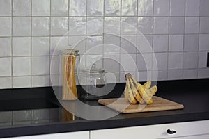 A portrait of a bunch of yellow bananas lying on a wooden cutting board on a black kitchen countertop. The delicious energizing