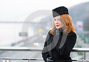 Portrait of business lady has rest on balcony. Aged women model in black coat and gloves. Woman on bridge waiting for meeting.