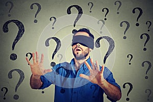 Portrait business man blindfolded stretching his arms out walking through many questions