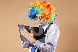 Portrait of business man in clown wig using a tablet to access t