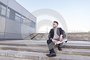 Portrait of a business man sitting on the street with coffee and documents in his hands and looking away