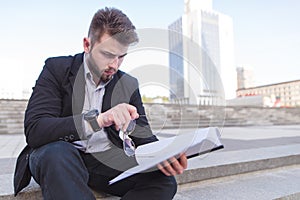 Portrait of a business man sitting on the street on the stairs and reading papers in his hands